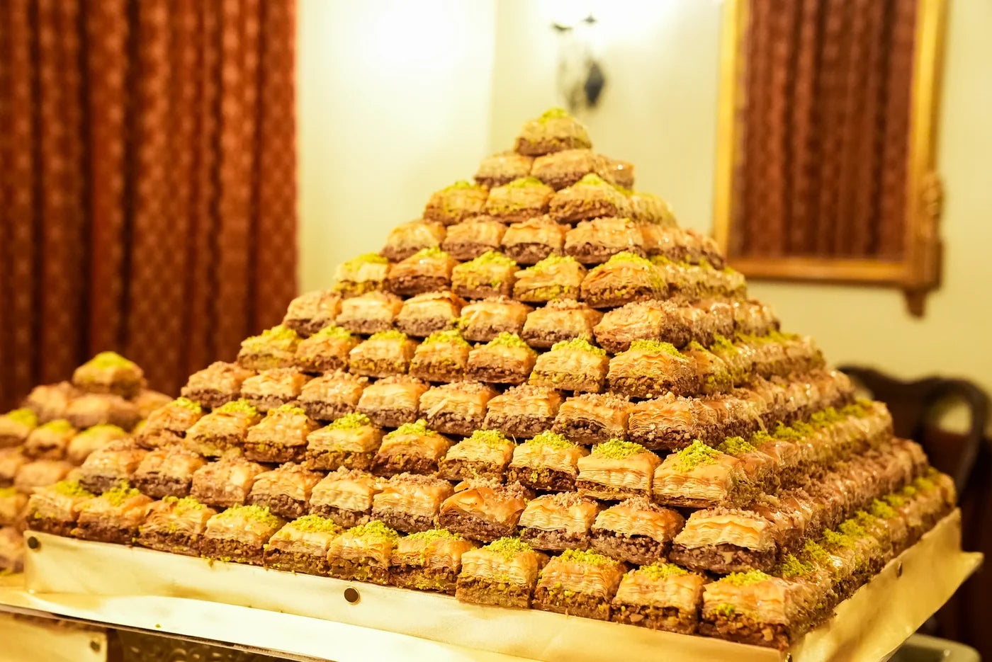 Baklava stacked into a large pyramid on a gold serving tray.